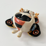 Ceramic sculpture of a small character with a large head wearing a Mothra costume, with a hood hat and a large set of wings behind it matching Mothra's colorways.